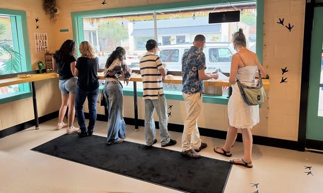 Customers standing at the window counter inside Acosta's, teal walls and a yellow bar looking out onto Glenn Ave